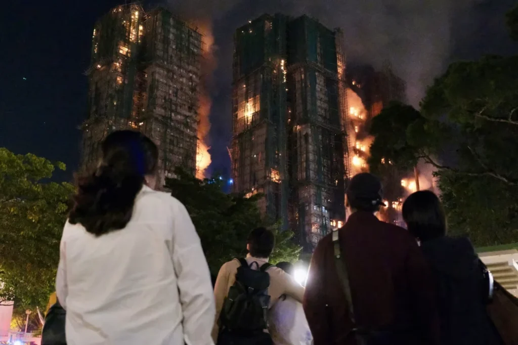 People look on as thick smoke and flames rise during a major fire at the Wang Fuk Court residential estate.