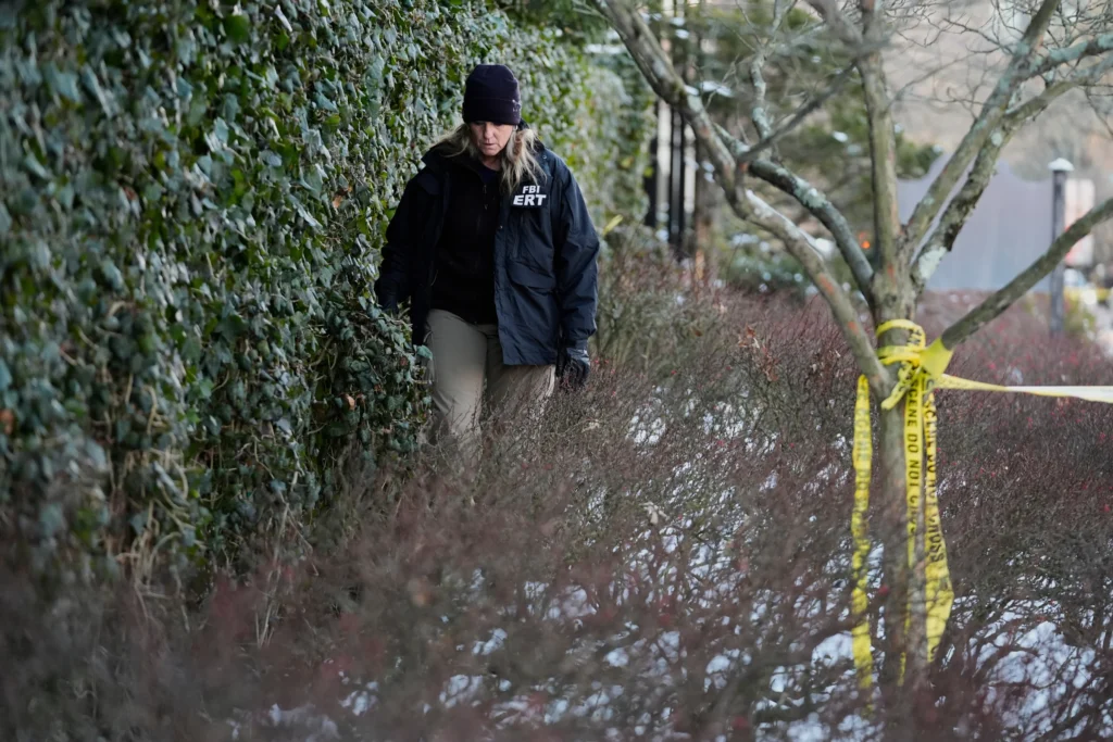 A member of the FBI Evidence Response Team searches for evidence near an ivy-covered wall, Monday, Dec. 15, 2025, in Providence, R.I.
