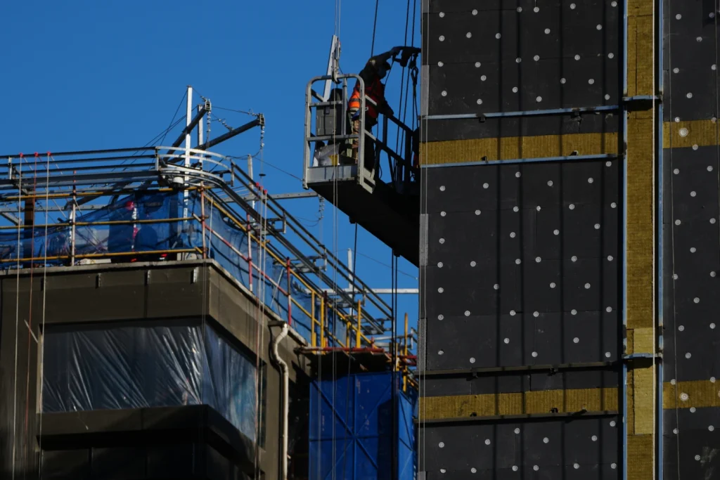 A worker on a scaffolding installs insulation layers on a residential building under construction, in Beijing