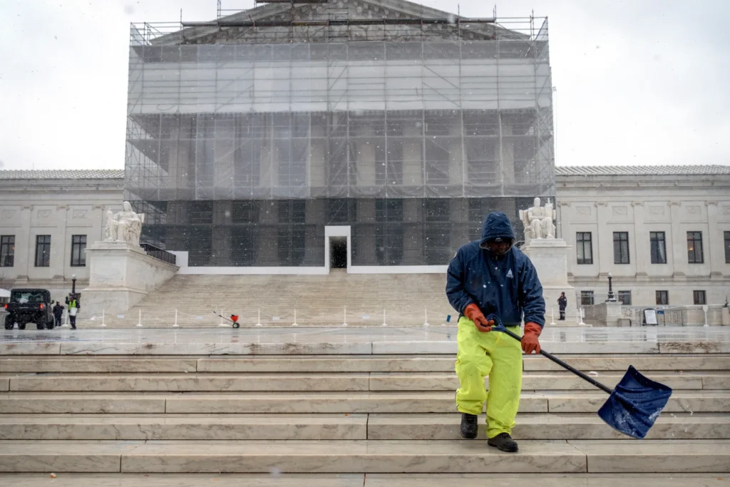 A worker shovels ice and snow in front of Supreme Court building during the first snowfall of the winter season in Washington