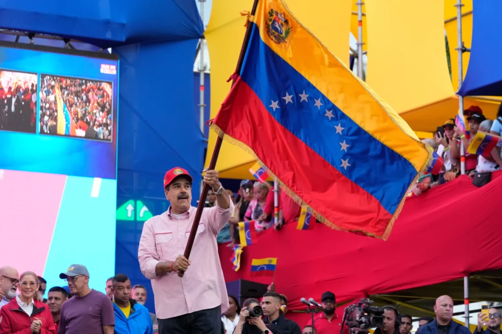 President Nicolas Maduro waves a Venezuelan flag during a swearing-in event for government-organized community committees at the presidential palace in Caracas, Venezuela, Monday, Dec. 1, 2025