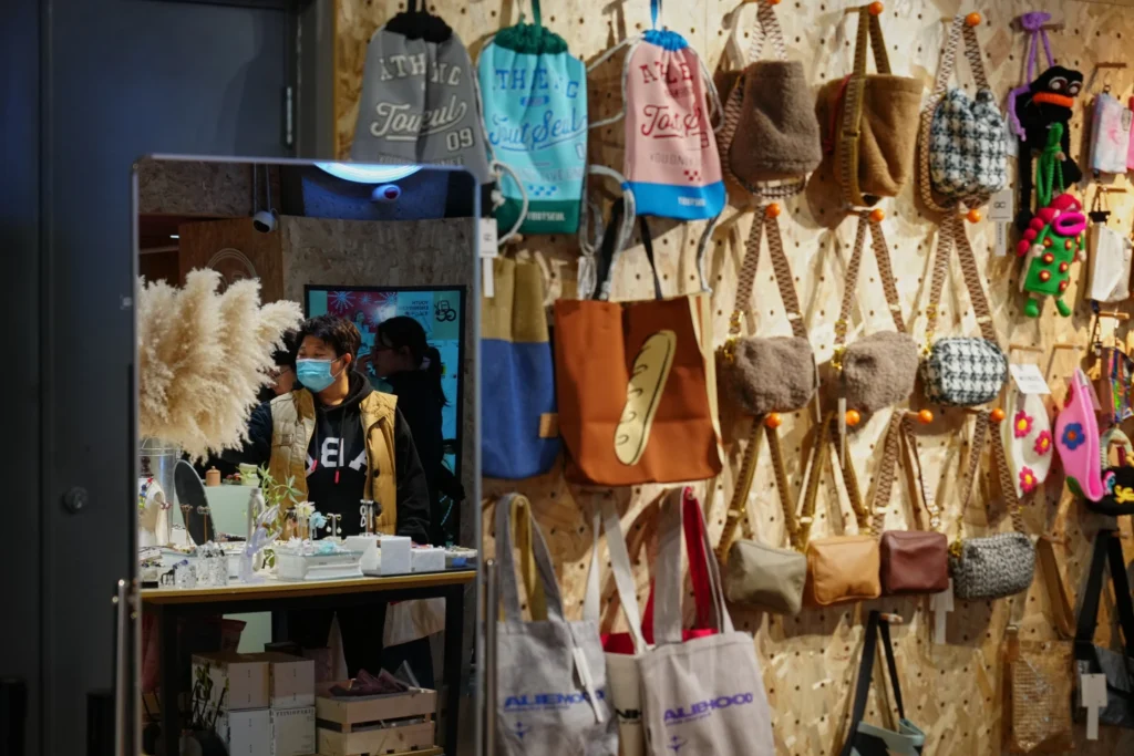 Shoppers are reflected on a mirror of a store selling fashion accessories and bags inside a shopping mall, in Beijing